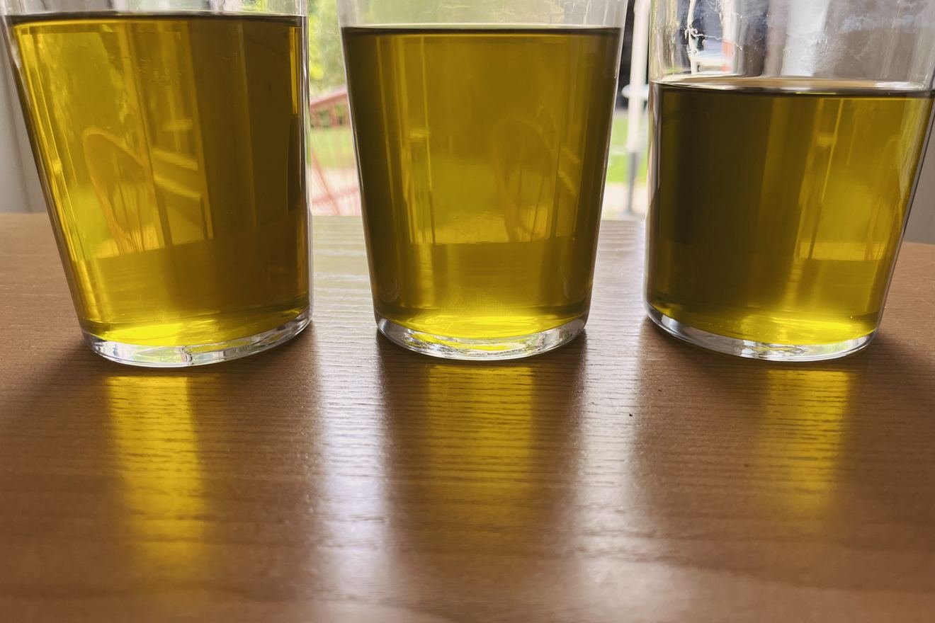 Les trois verres d'huile après le filtre à café, en contre-jour devant une baie vitrée : trois teintes dorées très proches.